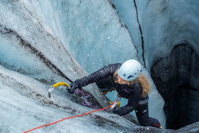 Ice Tunnel Solo Climber Female in white helmet climbing upwards from ice tunnel with yellow ice axes