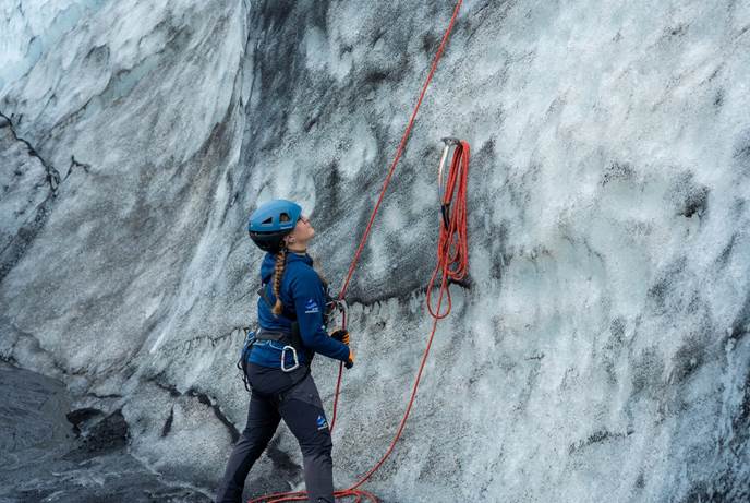 Grey White Pattern Glacier Female with orange safety rope standing at bottom of grey and white ice pattern glacier