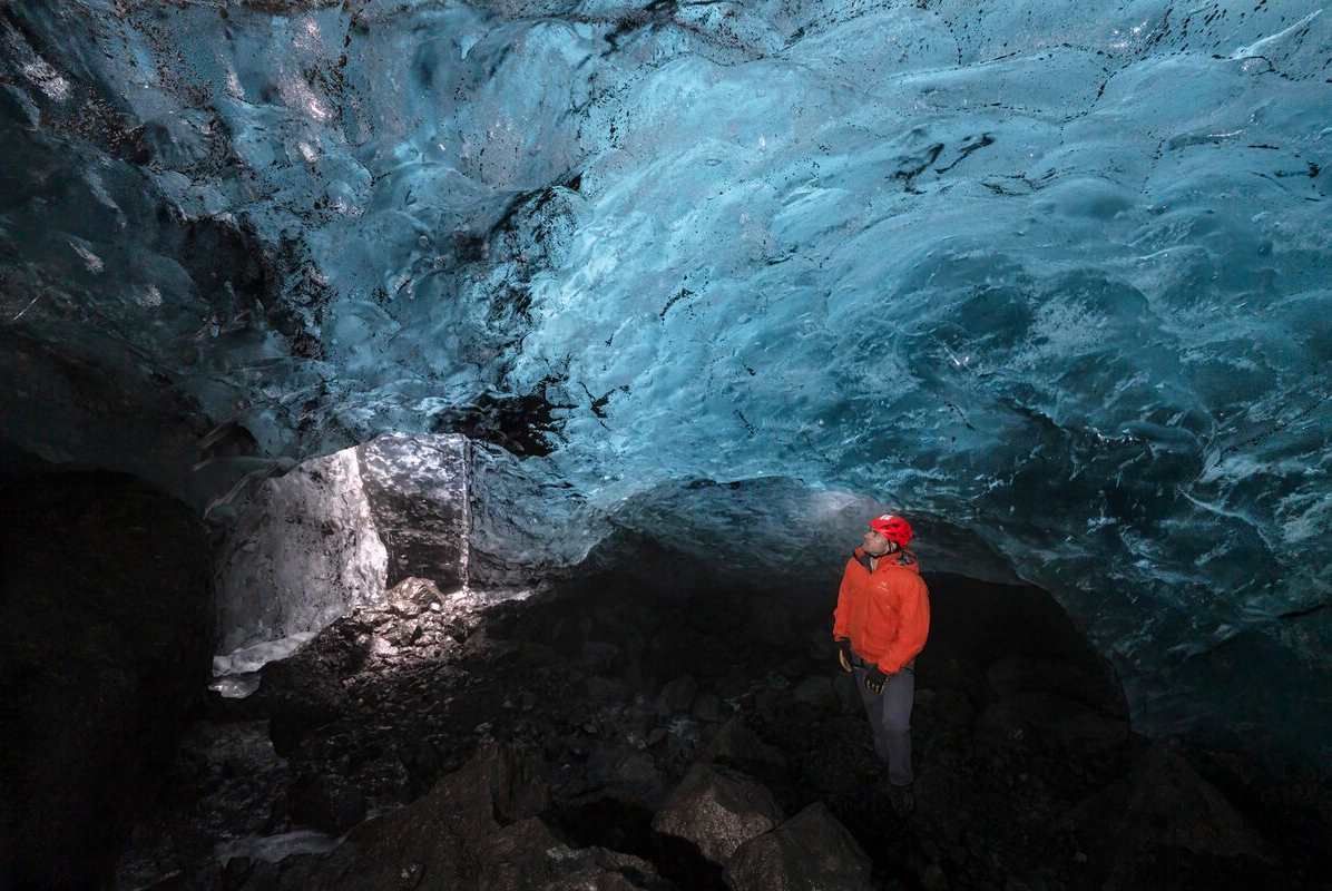 Male wearing bright red exploring inside Azure ice cave.