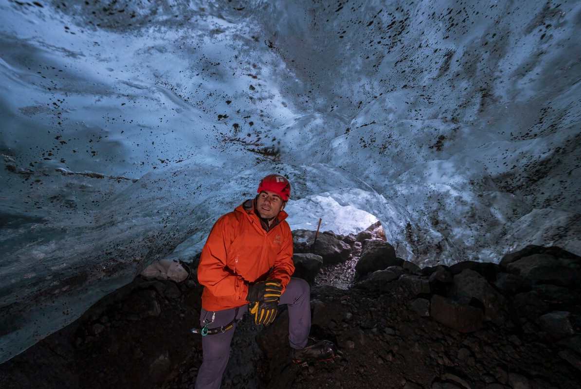 Male dressed in bright red posing inside Solheimajokull ice cave.