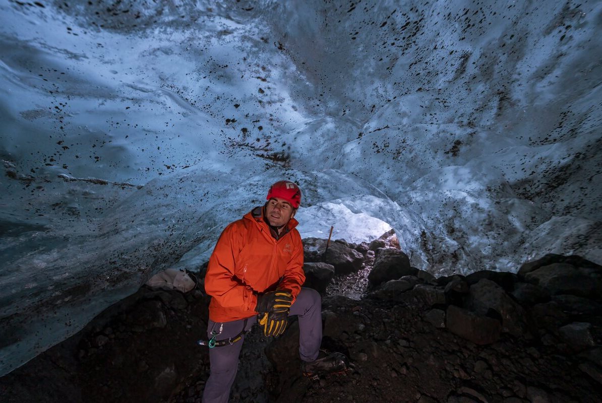 Male dressed in bright red posing inside Solheimajokull ice cave.