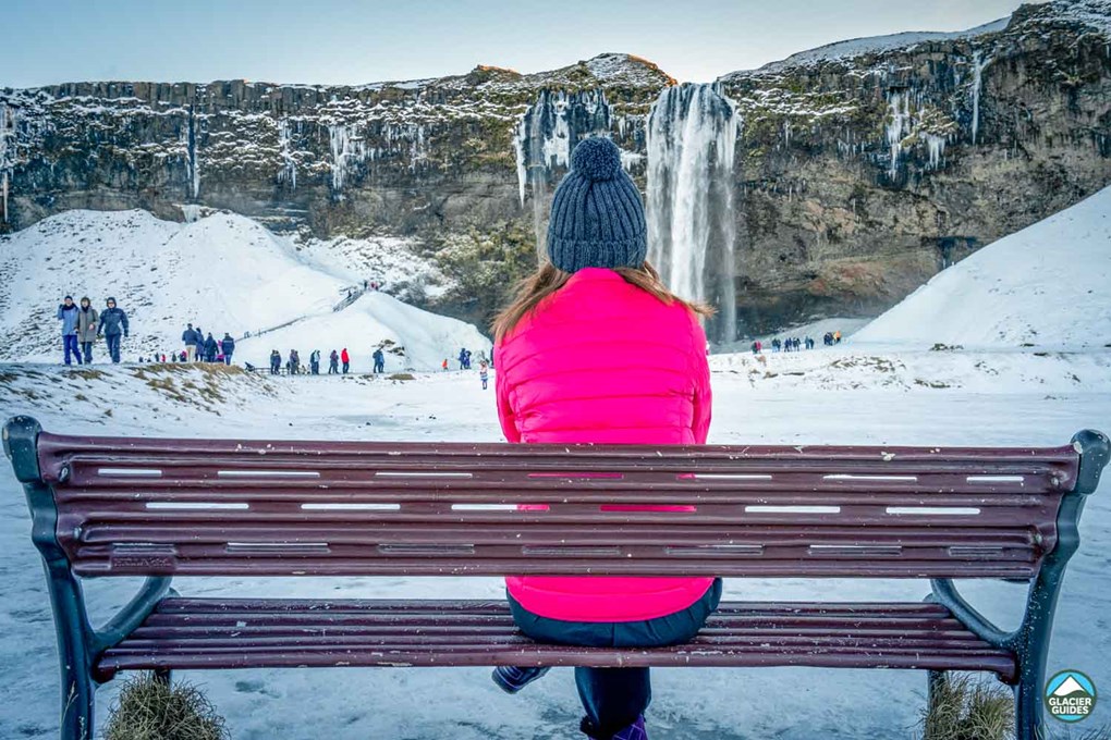 Girl On Bench Near Seljalandsfoss Waterfall In Winter