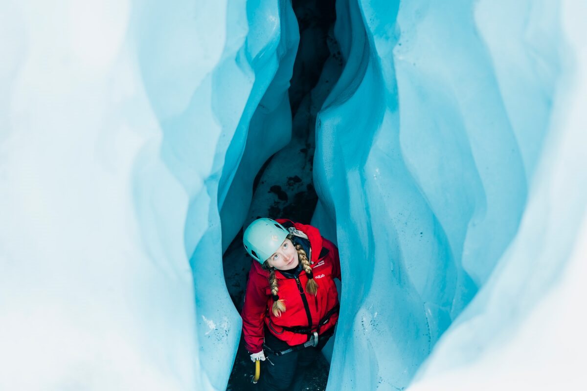Female tourist exploribng blue ice crevasse during ice climb.