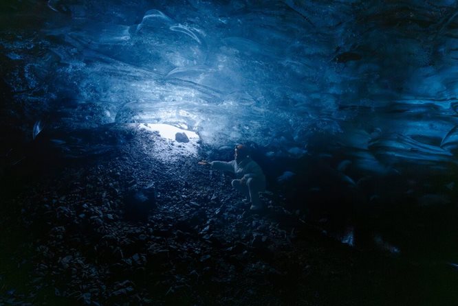 Woman crouching down inside beautiful blue ice cave