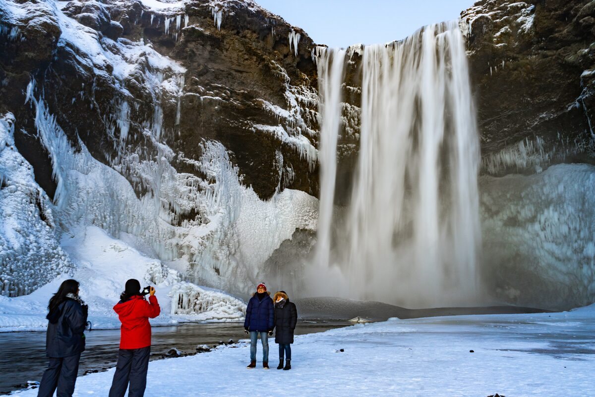 tourists taking photos in front of skogafoss waterfall in winter in iceland