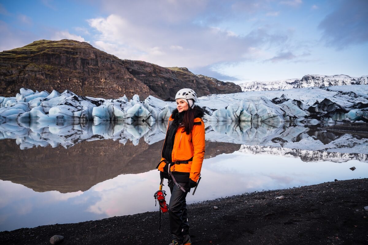 woman in an orange jacket in front of a glacier lagoon in iceland